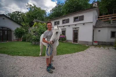 a man holding a white horse in front of a house at Tmbin's barn - nature, horses, family in Sežana