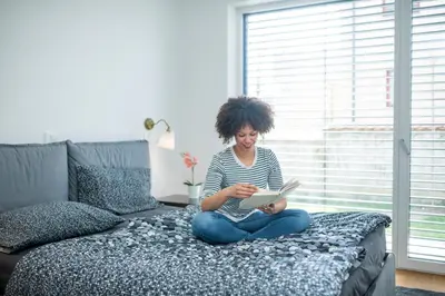a woman sitting on a bed reading a book at Apartments Villa Popp in Ljubljana