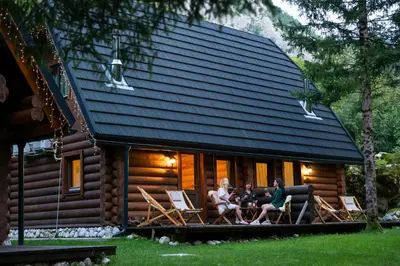 three people sitting on the porch of a log cabin at Pristava Lepena Village in Lepena