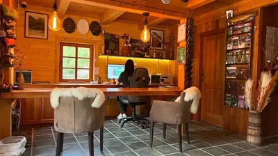 a woman sitting at a desk in a kitchen with chairs at Pristava Lepena Village in Lepena
