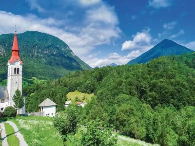 a church on a hill with mountains in the background at Počitniška hiša Pri Kuštrču in Grahovo