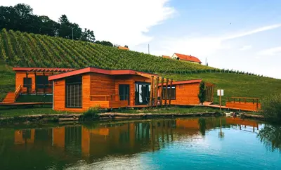a wooden cabin next to a river with a hill at Naturasort Holiday Houses in Pesnica pri Mariboru