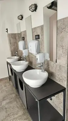 a bathroom with three sinks and two mirrors at AdHoc Hostel in Ljubljana