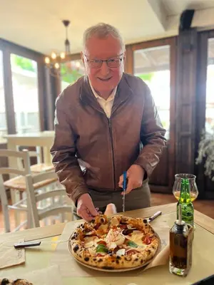 an older man cutting into a pizza on a table at Hotel Katrca in Ljubljana