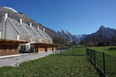 a barn with a fence next to a field and mountains at ALPIN apartma in Bovec