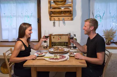 a man and woman sitting at a table with wine glasses at ETNO HOUSE GOSTECE- Suite with Finnish sauna in Mozirje