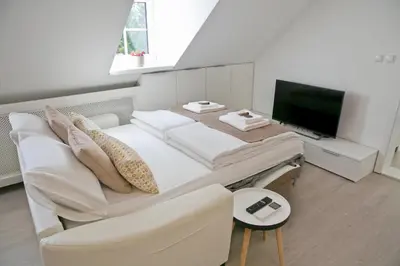 a white bedroom with a large bed and a tv at Apartments Hiša Pod Gradom in Ljubljana