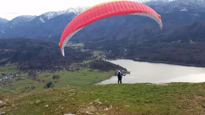 a person flying a red parachute over a lake at Snežak (Snowman) in Bohinj
