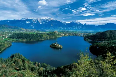 an island in the middle of a lake with mountains at Apartments Vidic in Bled