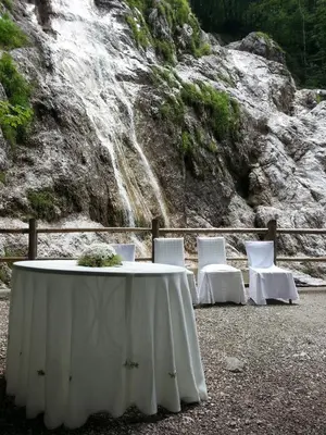 a table and chairs with a waterfall in the background at Hotel Plesnik Logar Valley in Solčava