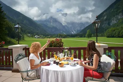 two women sitting at a table on a balcony at Hotel Plesnik Logar Valley in Solčava