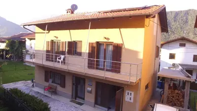 a yellow house with a dog sitting on a balcony at Apartment Green Valley in Idrsko