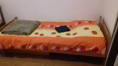 a small bed with an orange and white comforter at Apartment Green Valley in Idrsko