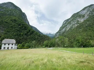a white house in a field with mountains in the background at Apartments and rooms Nataša 2 in Trenta