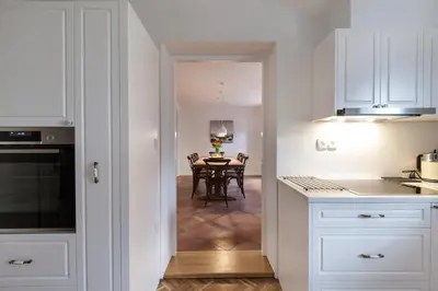 a kitchen with white cabinets and a dining room with a table at River and Castle View Apartment Rose Tour As Ljubljana in Ljubljana