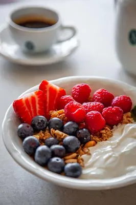 a bowl of yogurt and berries with a cup of coffee at Hotel Slamič Ljubljana in Ljubljana