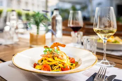a plate of pasta with shrimp on a table with wine glasses at Hotel Slamič Ljubljana in Ljubljana