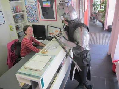a woman sitting at a desk with a statue of a man in armour at MCC Hostel in Celje