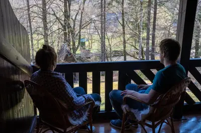 two people sitting in chairs watching a giraffe through a window at TUBA Apartments in Bohinj