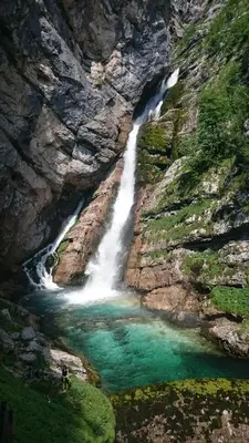 a waterfall on the side of a mountain with green water at Hike & Bike Chalet in Bohinj