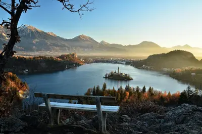 a bench on a hill overlooking a river with a boat at Hostel Bled Paradise Slovenia in Bled-Rečica