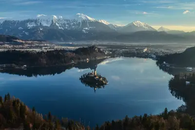 an island in the middle of a lake with snow capped mountains at Hostel Bled Paradise Slovenia in Bled-Rečica