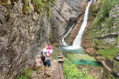 a family standing on a bridge in front of a waterfall at Apartments & Hostel Bohinj in Bohinj