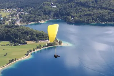 a person riding a yellow parachute over a body of water at Apartments & Hostel Bohinj in Bohinj