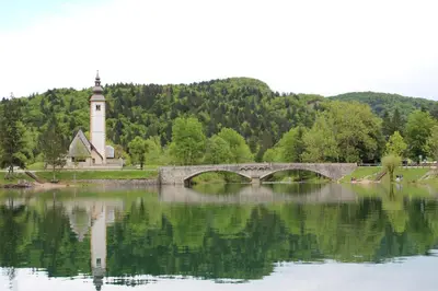 a bridge over a lake with a building and a clock tower at Apartments Na Vasi in Bohinj