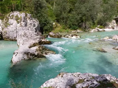 a river with blue water and rocks and trees at The Millhouse Bled in Bled