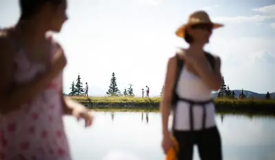 a woman in a hat standing next to a body of water at Lake Peak Apartments, Ribniško Pohorje in Ribnica na Pohorju