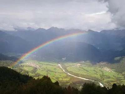 a rainbow over a green valley with a river at Nebesa Chalets in Kobarid