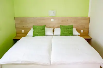 a large bed with white sheets and green pillows at Rooms Šajina in Podgrad