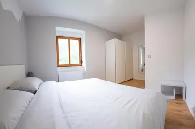a white bedroom with a white bed and a window at Hiša Urška in Log pod Mangartom