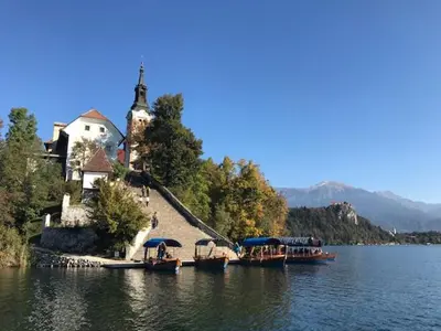 a church on the shore of a lake with boats at Adventure Cottage with pool and big garden in Bled