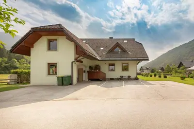 a white house with a brown roof and a driveway at APARTMA KOŠNIK in Bohinj
