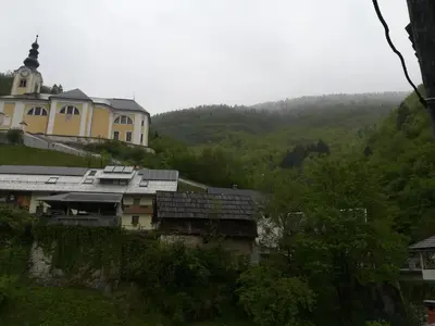 a large yellow building on a hill with a church at Apartma PR PEKOVCU in Bohinj