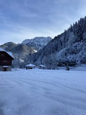 a snow covered field with a house and mountains at Turistična kmetija Čerček in Solčava
