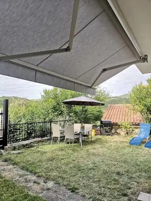 a patio with an umbrella and chairs and a grill at Appartma Katja in Gabrovica pri Črnem Kalu