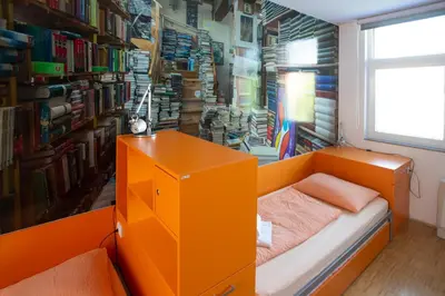 a bedroom with an orange bed and a book shelf at Hostel Pekarna in Maribor