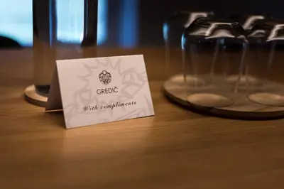 a white card sitting on a table next to two glasses at Gredič Heritage Residences in Dobrovo