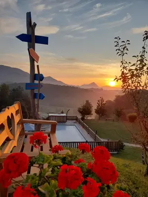 a cross and a bench and red flowers with the sunset at Relax Guest House Marjanca in Rogaška Slatina
