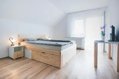 a white bedroom with a bed and a wooden floor at Apartma pri Boštjanu in Škofja Loka