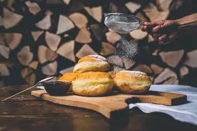 a person sprinkling powdered sugar on rolls on a cutting board at Apartma pri Boštjanu in Škofja Loka