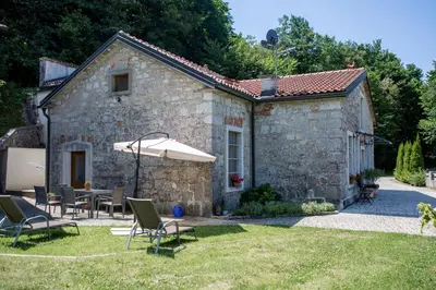 a stone house with a table and chairs and an umbrella at Villa Anton - The Old Dairy in Hrušica