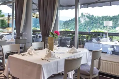 a restaurant with white tables and chairs and a large window at Hotel Kompas in Bled