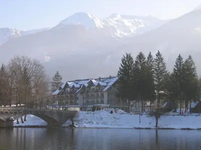 a building on a bridge over a lake with snow covered mountains at Hotel Jezero in Bohinj