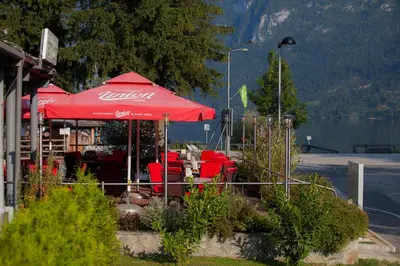 a restaurant with a red umbrella and red chairs at Hotel Jezero in Bohinj