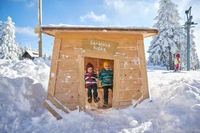 two children are sitting in a wooden dog house in the snow at Hotel Planja in Zreče