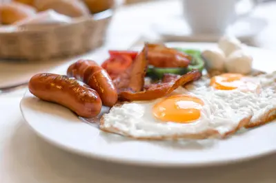 a plate of breakfast food with eggs sausage and bacon at Hotel Bau Maribor in Maribor